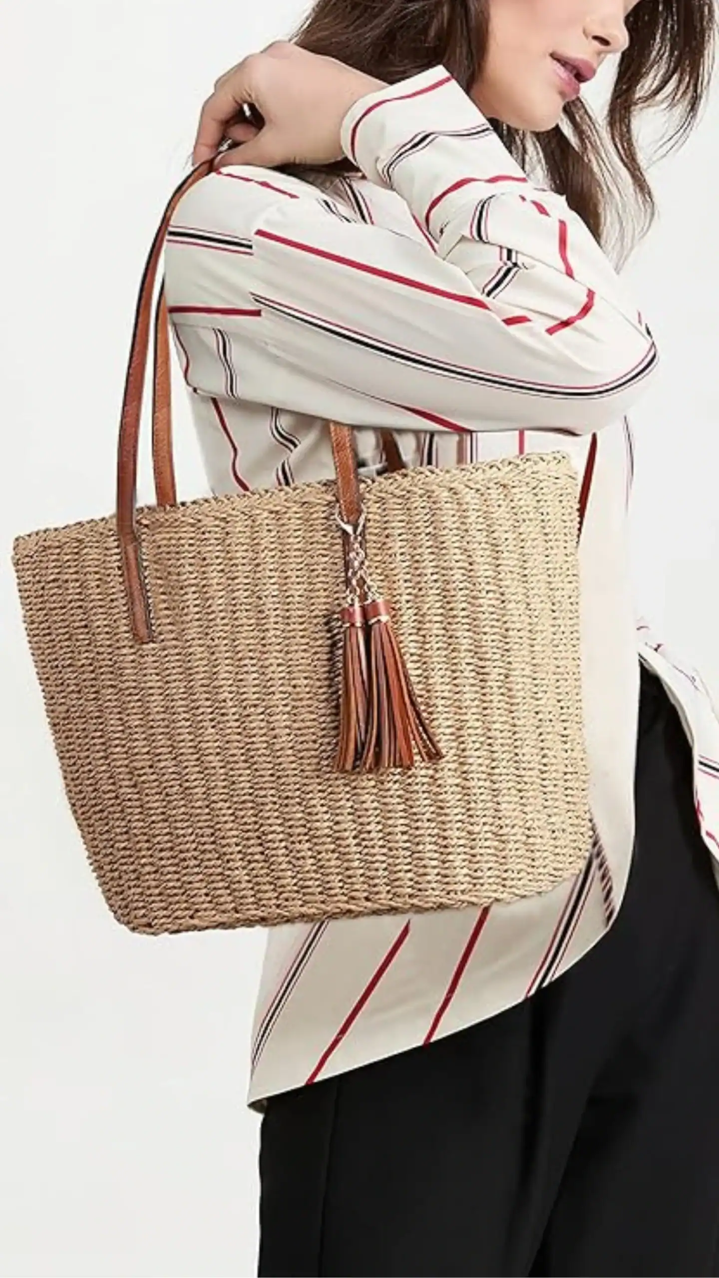 The handbag features a relaxed tote silhouette with a large, rectangular shape, made from textured woven straw in a natural beige tone. It is complemented by structured brown leather handles and a matching tassel, exuding a casual yet chic vibe suitable for everyday use or sunny outings.