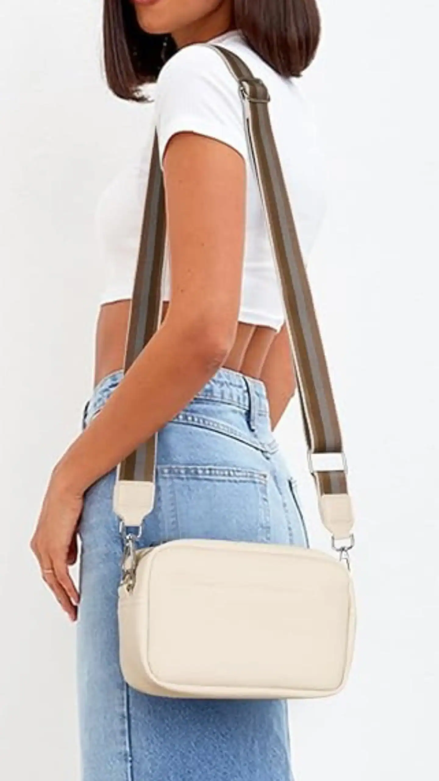 The bag features a rectangular silhouette with a smooth, matte faux leather finish in a soft, cream color, complemented by a thick, contrasting guitar strap in brown with neutral accents. Its minimalist design exudes a casual and trendy vibe, making it ideal for everyday outings or relaxed social events.