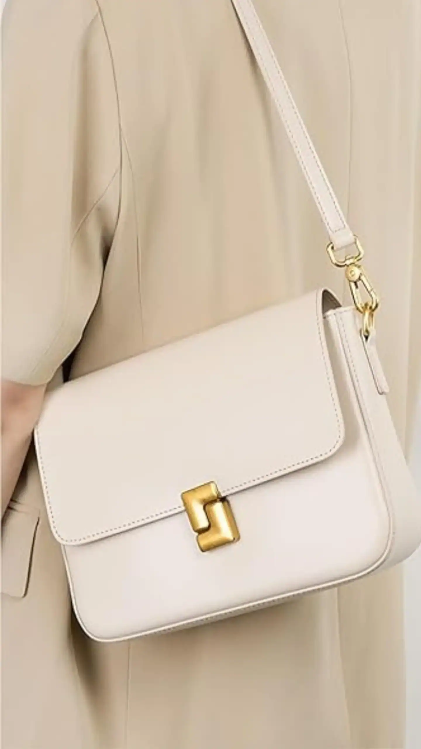 This elegant shoulder bag features a structured silhouette with a sleek, minimalist design made from luxury genuine leather, offering a smooth, matte texture. It is a soft beige color and showcases a striking gold clasp embellishment, making it perfect for both casual outings and formal events.