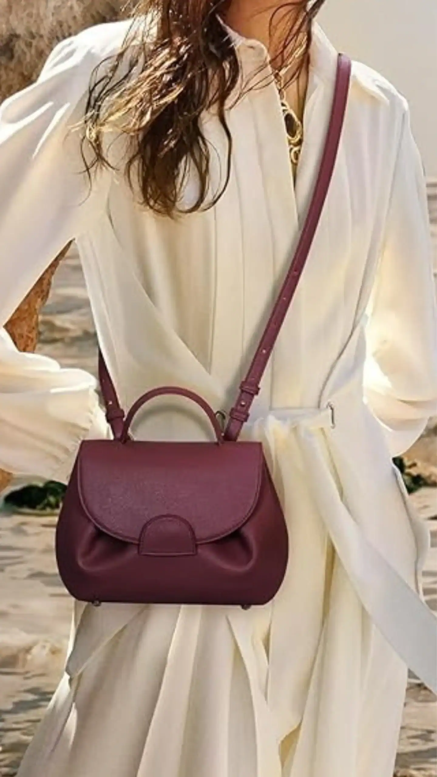 A luxury mini faux leather handbag in a rich burgundy color, featuring a structured silhouette with a soft, curved flap and a delicate bow-like embellishment at the base. The adjustable crossbody strap enhances its versatility, making it suitable for both casual outings and more formal occasions, exuding a minimalist and chic vibe.