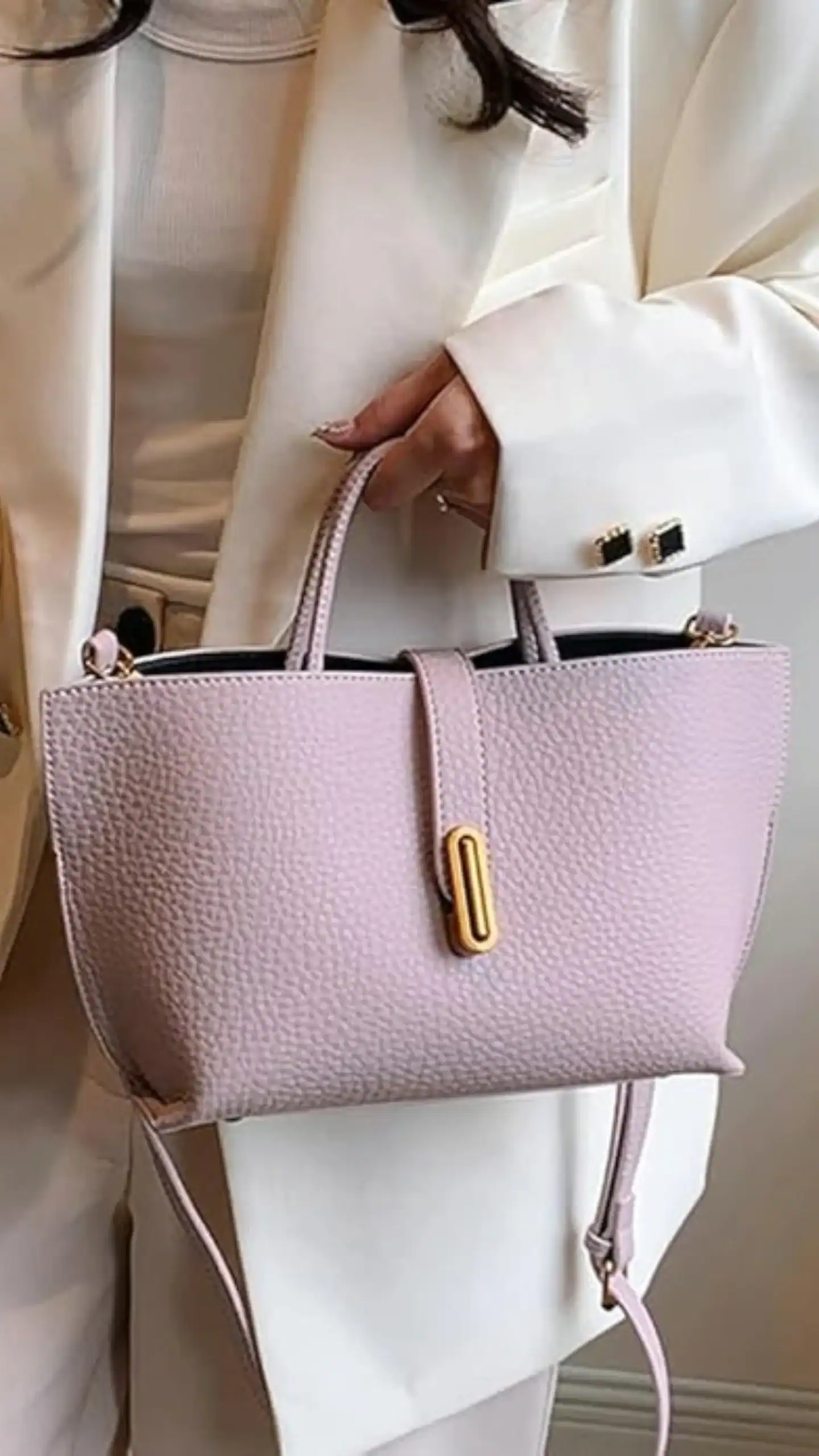 This hobo handbag features a structured silhouette with a soft, slouchy design made of textured vegan leather. Its delicate pastel lavender color is complemented by a sleek gold buckle accent, exuding a modern and chic vibe ideal for casual outings or everyday use.