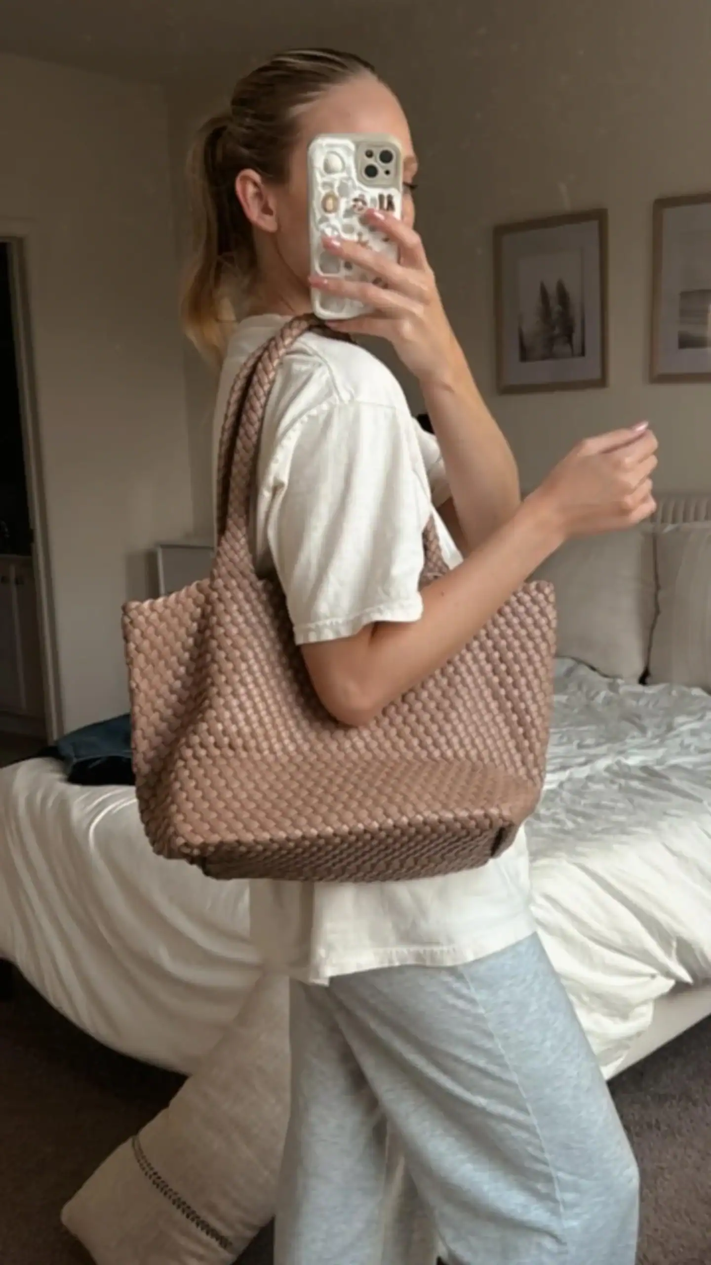 A large, woven tote bag in a soft, muted rose hue, crafted from vegan leather, featuring a textured finish that enhances its luxurious appearance. This versatile and stylish handbag, ideal for casual outings or beach days, has a relaxed silhouette with broad handles for easy carrying, exuding a chic yet understated vibe.