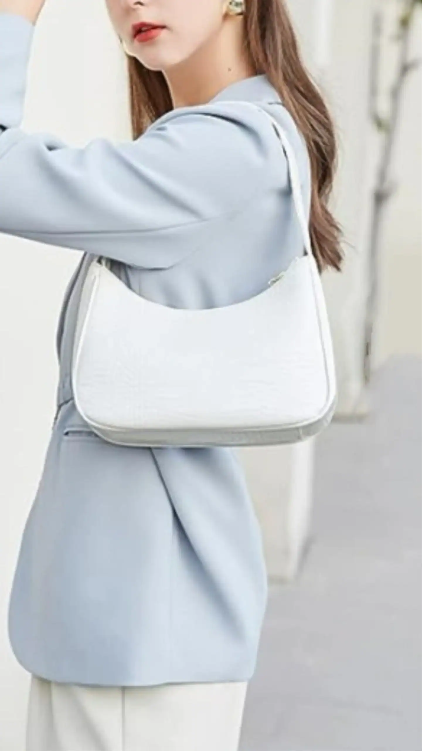 This white handbag features a sleek, curved silhouette crafted from embossed faux leather, offering a smooth, reptilian texture. Its minimalist design and neutral color make it ideal for casual outings or elevating a sophisticated look.