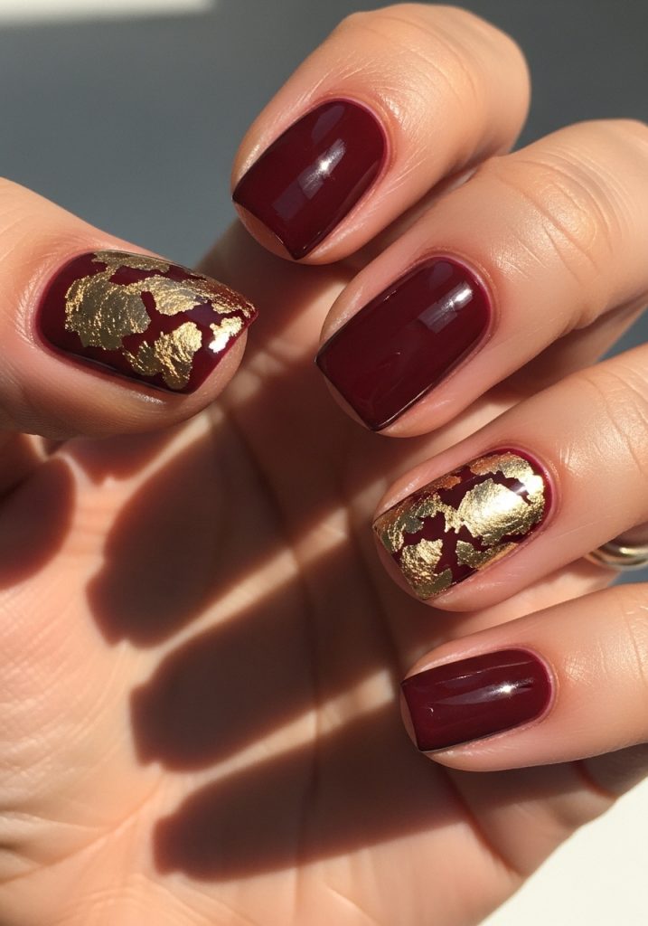 Burgundy nails with gold foil accents on two fingers with glossy finish