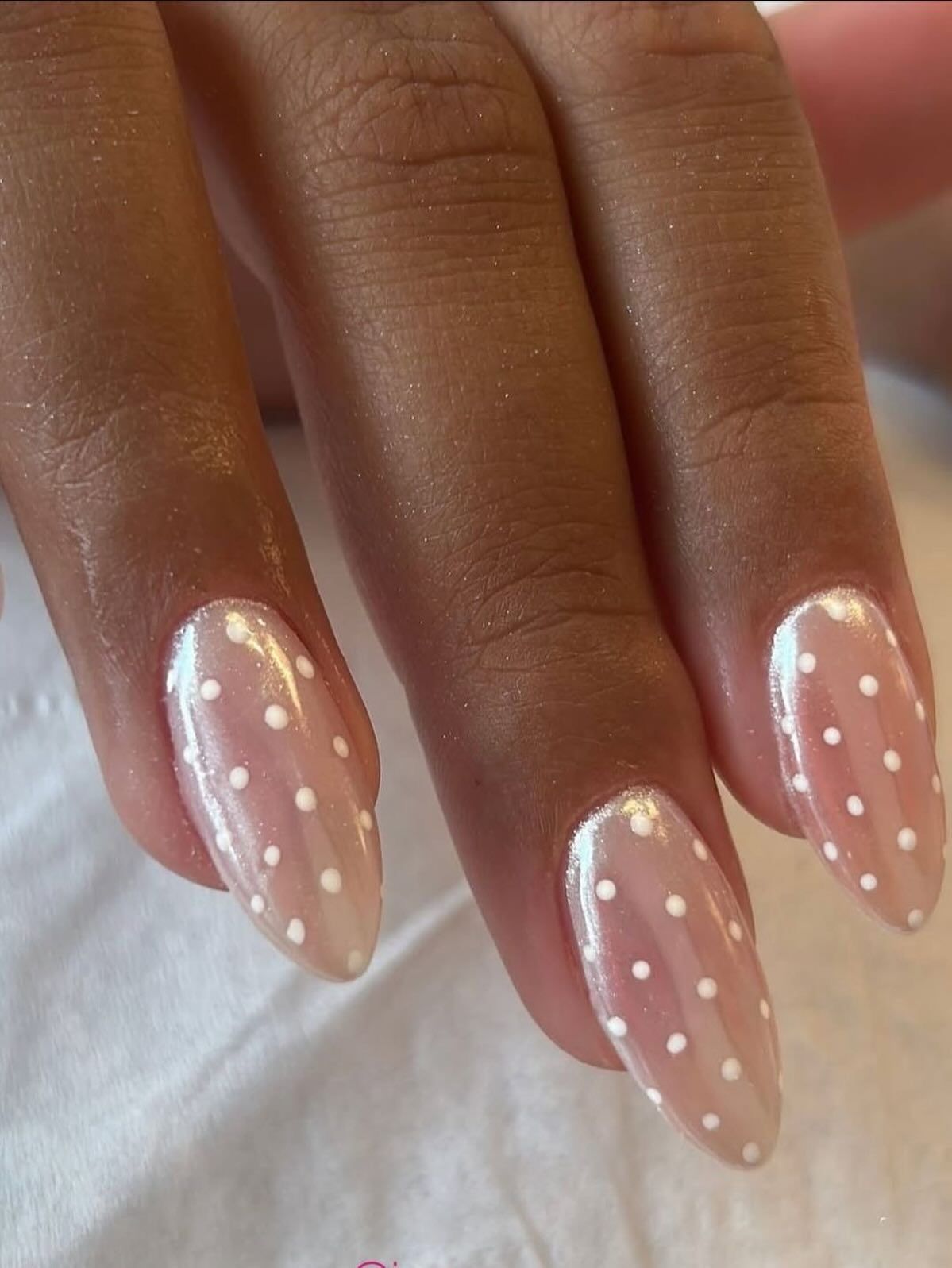 Close up of five almond shaped nails painted with a sheer iridescent polish and small white polka dots.