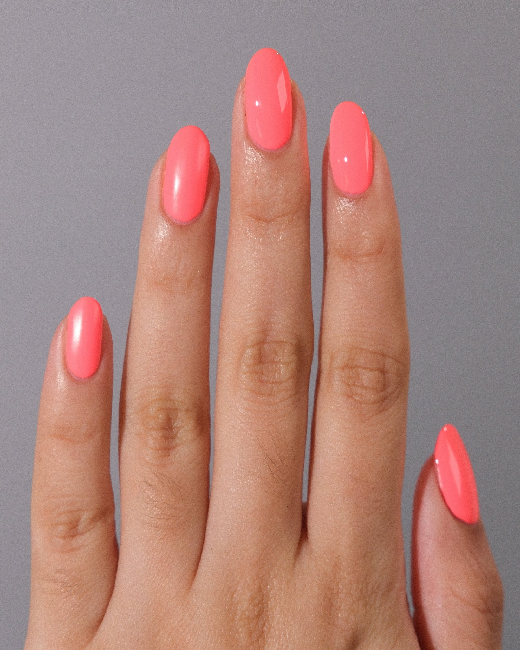 Hand with five fingers splayed, showing short almond-shaped nails painted a bright coral color.