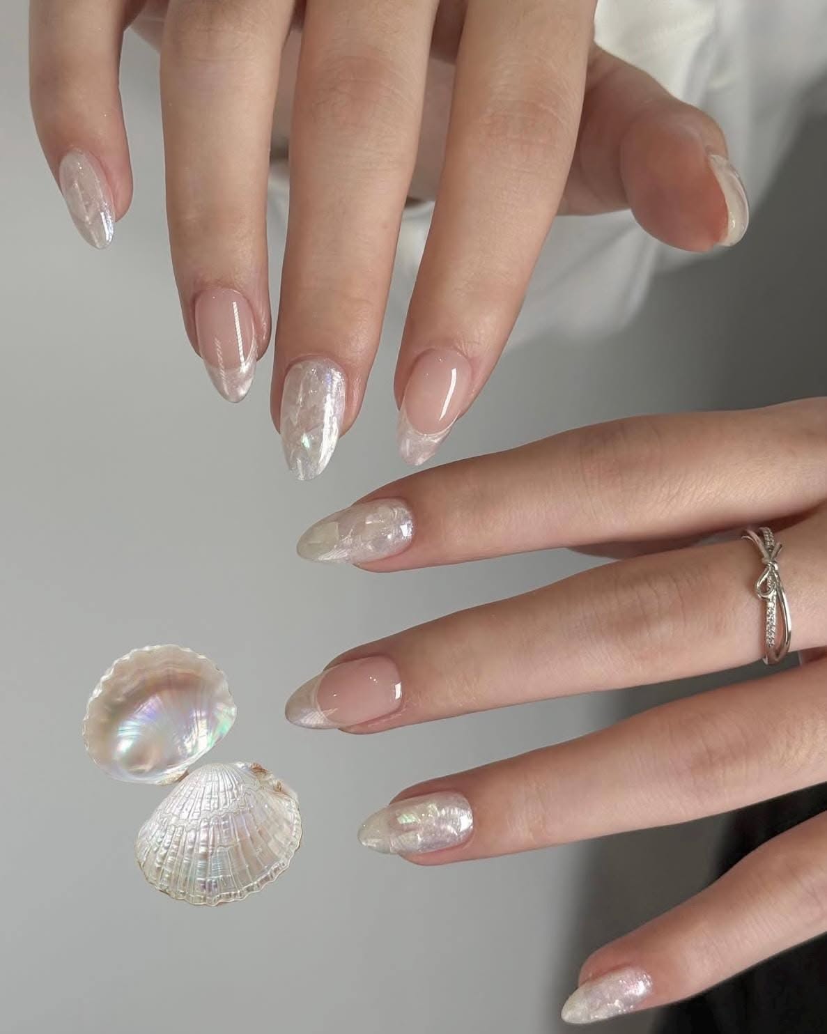A person's hands display long, almond-shaped nails with iridescent pearl French tips.