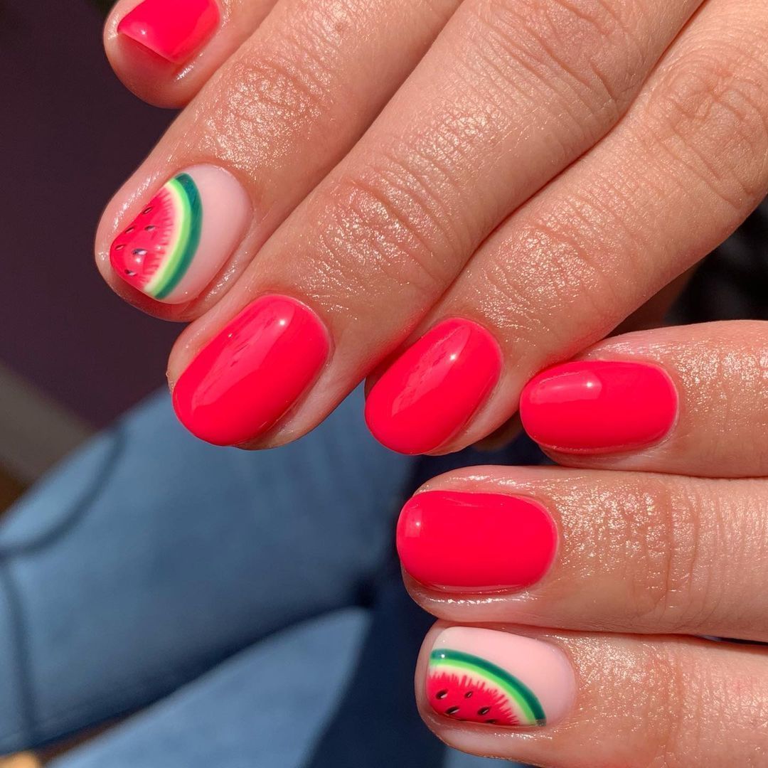 Close-up of fingers with bright pink painted nails and a single accent nail on each hand featuring half a watermelon design.