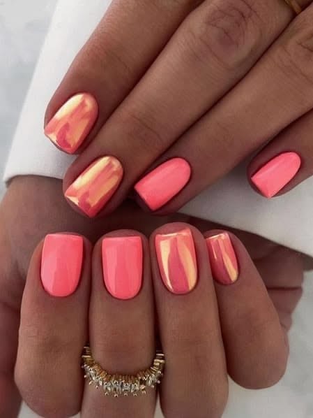 Close-up of a person's hands with coral-colored nails, some of which feature a shimmering iridescent chrome finish.