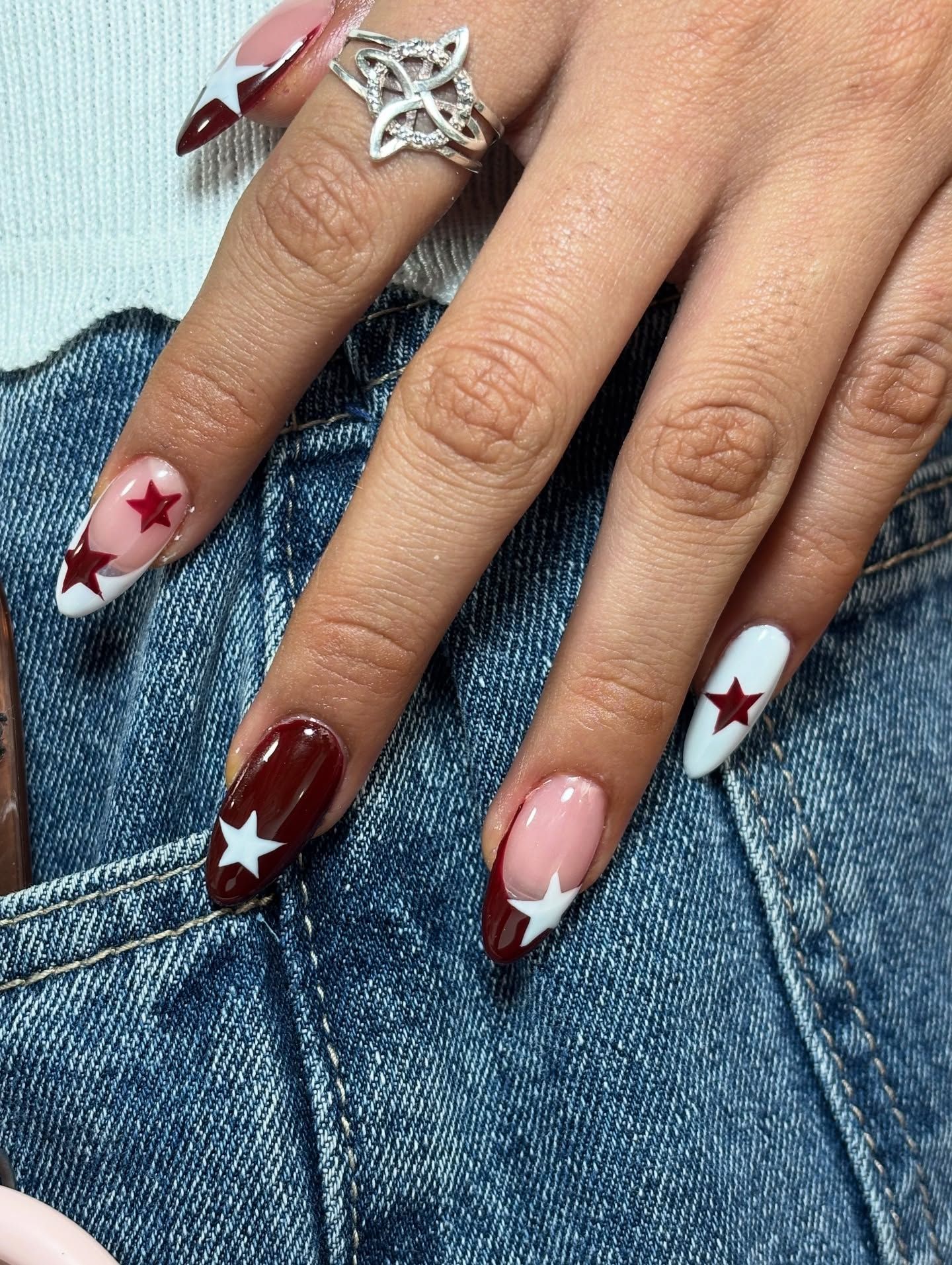 Hand with coffin-shaped nails featuring French tips in white and dark red, with star designs in alternating colors, against…