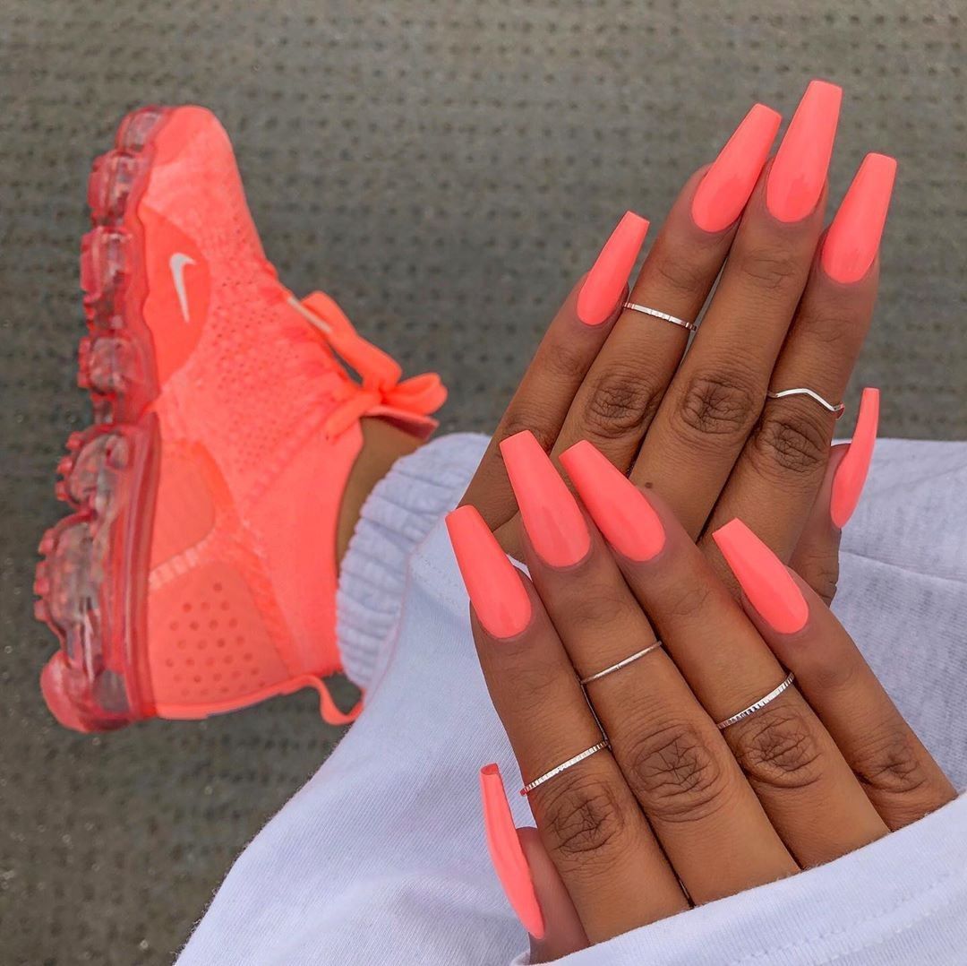 A person's hands with long coral square-tipped nails. Their hands are adorned with minimalist silver rings.