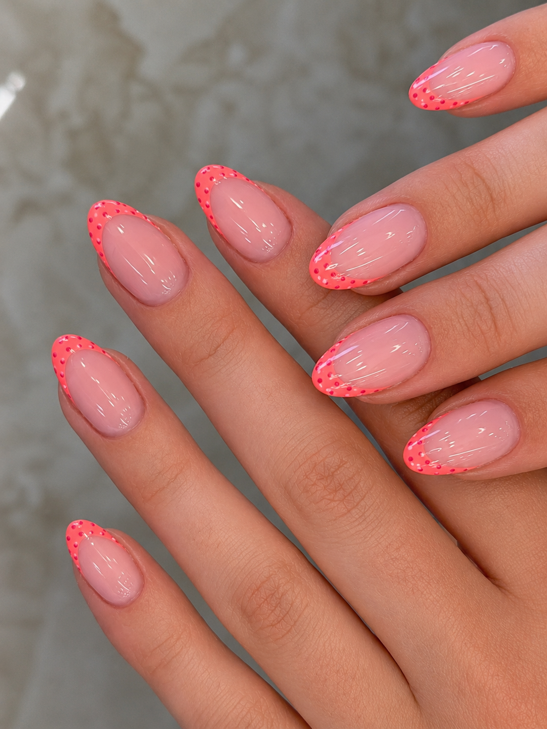 Close-up of a person's hands with an updated French manicure, featuring coral-colored tips with small red dots.