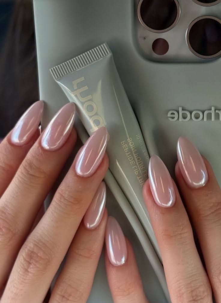 Hands with rose pink, pearl-finish almond nails holding a light grey tube of lip gloss.