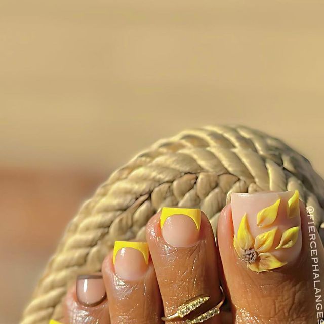 Close-up of a foot with a 3D yellow sunflower design on the big toe and yellow French tips on other toes