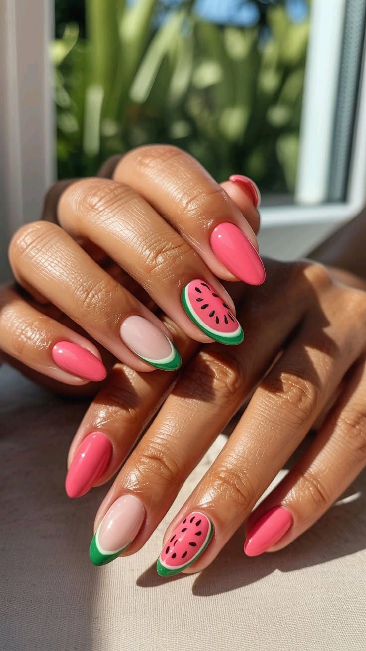 Close-up of a person's hands with watermelon-themed nail art. Some nails are solid pink, one has a watermelon slice, and…