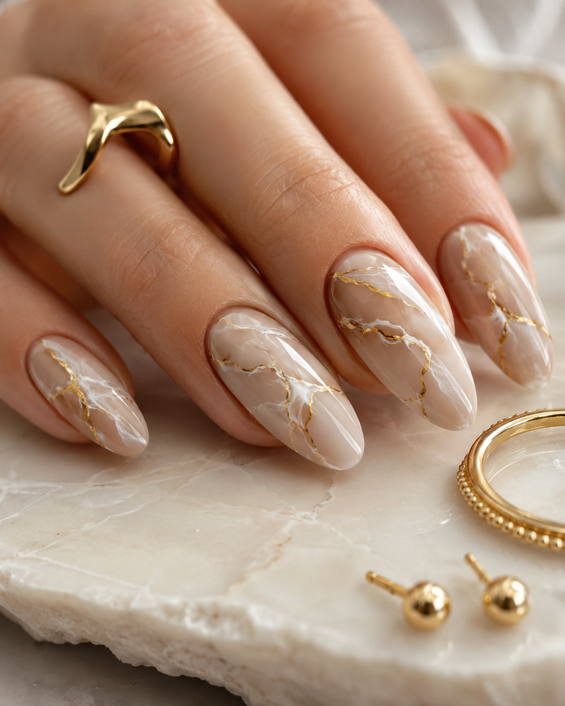 Close-up of a hand with nails painted in a warm, light beige marble pattern with thin gold lines.