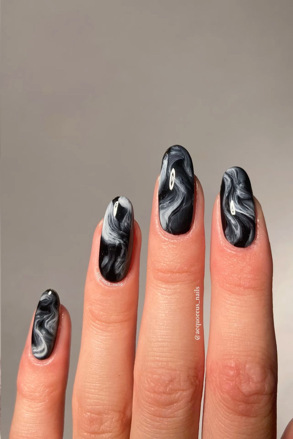 Close-up of a hand with four almond-shaped nails, each painted with a swirling black and white marble design.