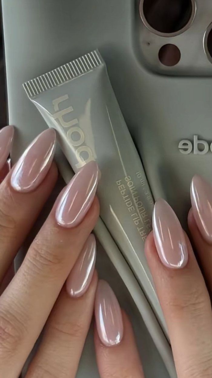 A person's hand shows almond-shaped fingernails with a pearlescent rose gold polish.