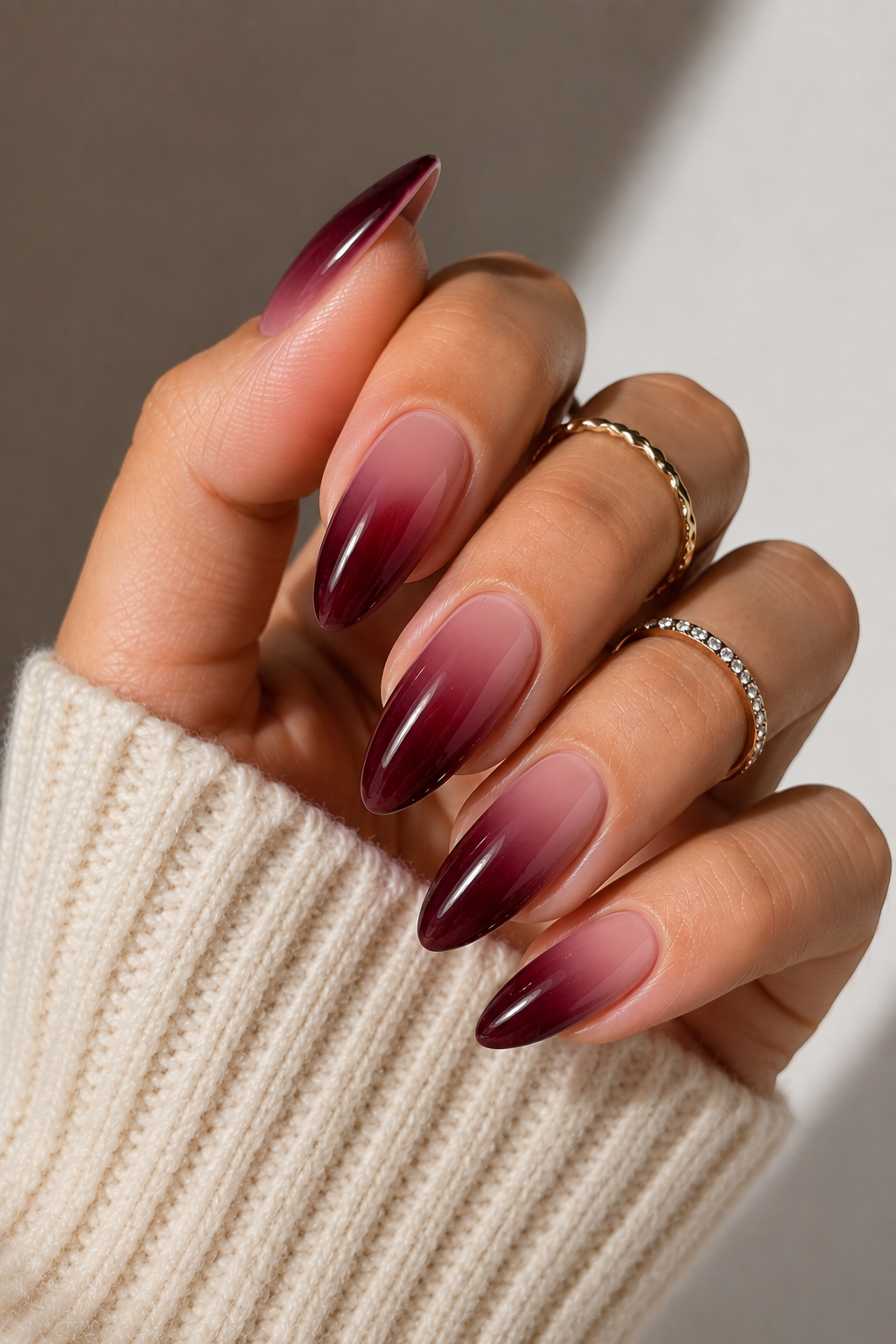 Hand with long almond-shaped nails featuring a dark burgundy ombre fading into a lighter, natural tone near the cuticle.