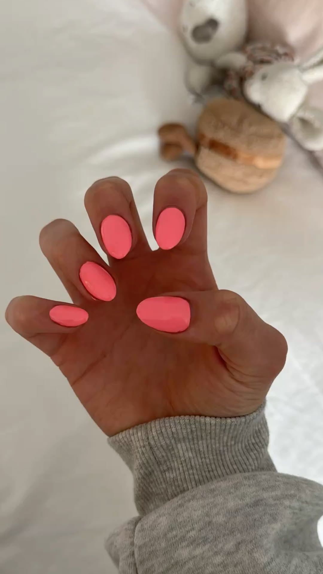Close up of a hand with short, oval shaped nails painted in a solid, bright coral color.