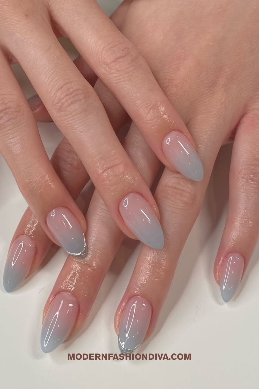 Close-up of hands with light pink and blue gradient ombre nails with almond shape, some nails have silver tips.