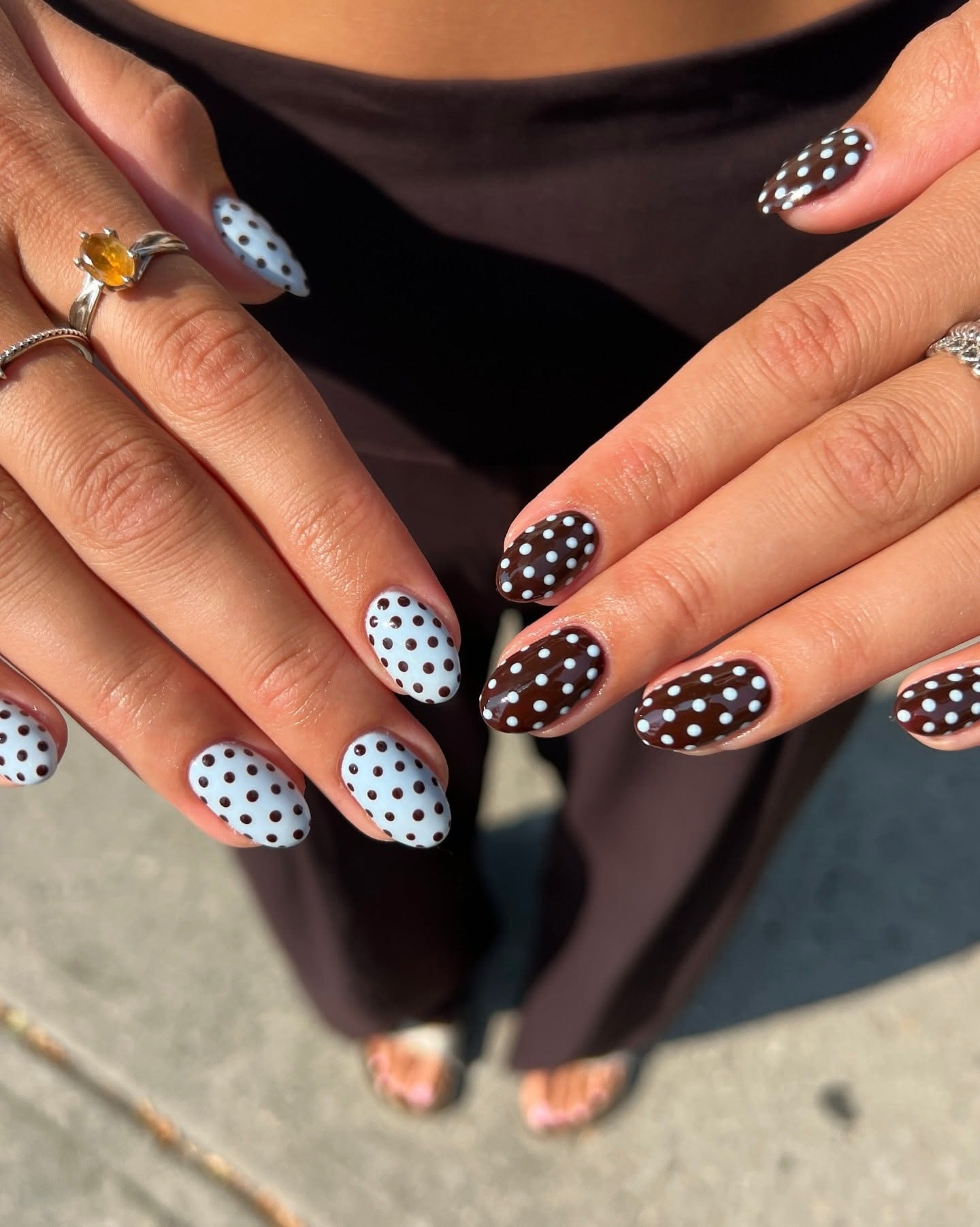 A person's hands display short oval nails with an alternating polka dot design: light blue nails with brown dots, and dark…