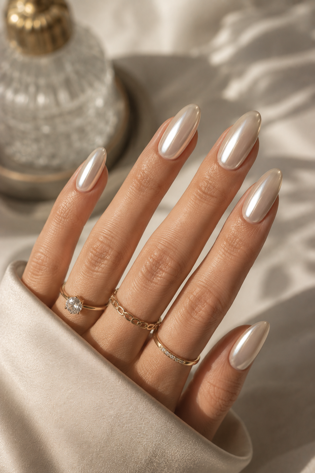 Hand with almond-shaped pearl chrome nails and gold rings on fingers