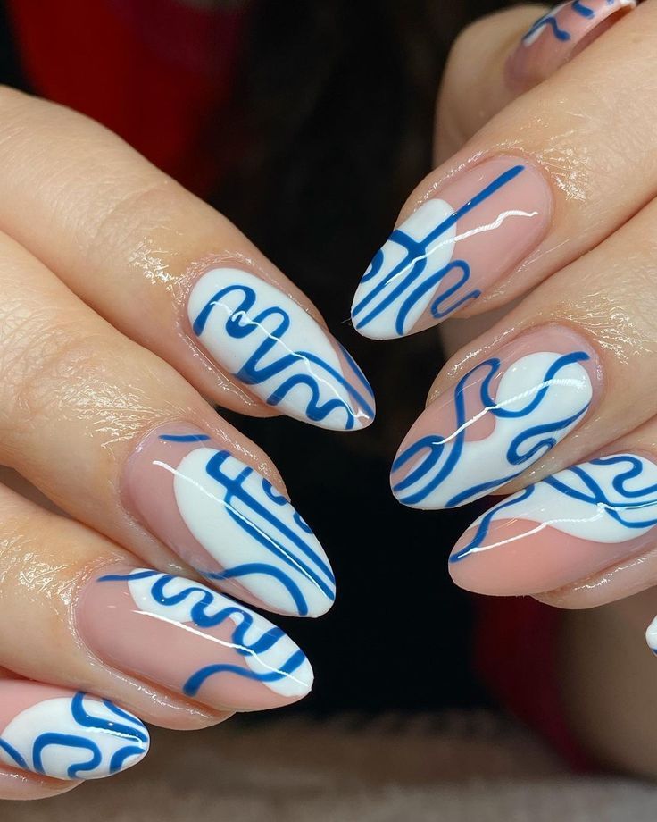 Close up of manicured hands with almond-shaped nails featuring blue abstract wavy lines over white and clear polish.