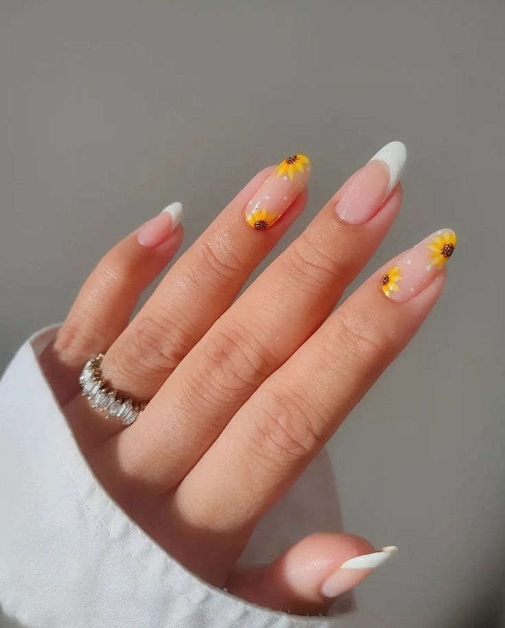 Hand with almond-shaped nails featuring white French tips on some fingers, and tiny painted sunflowers on others.