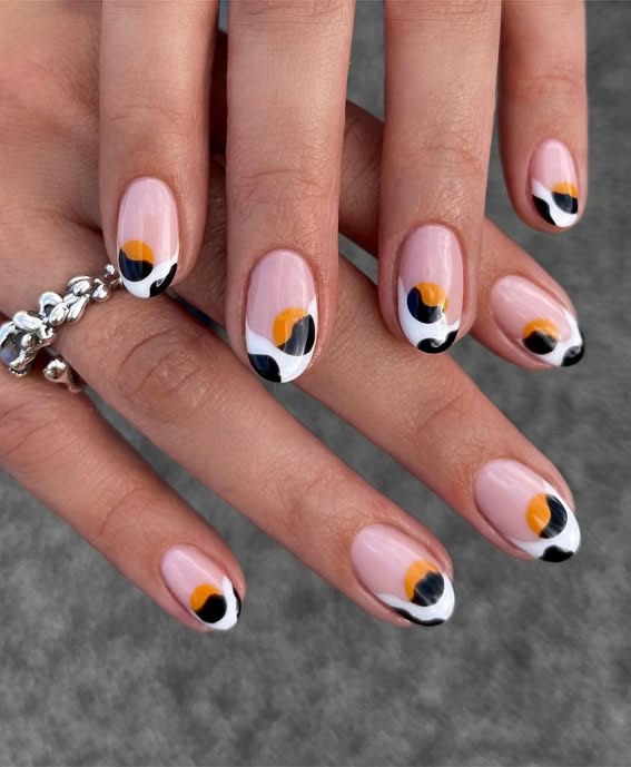 Close-up of a person's hands with an abstract nail art design featuring orange-yellow, black, and white swirls on a nude base