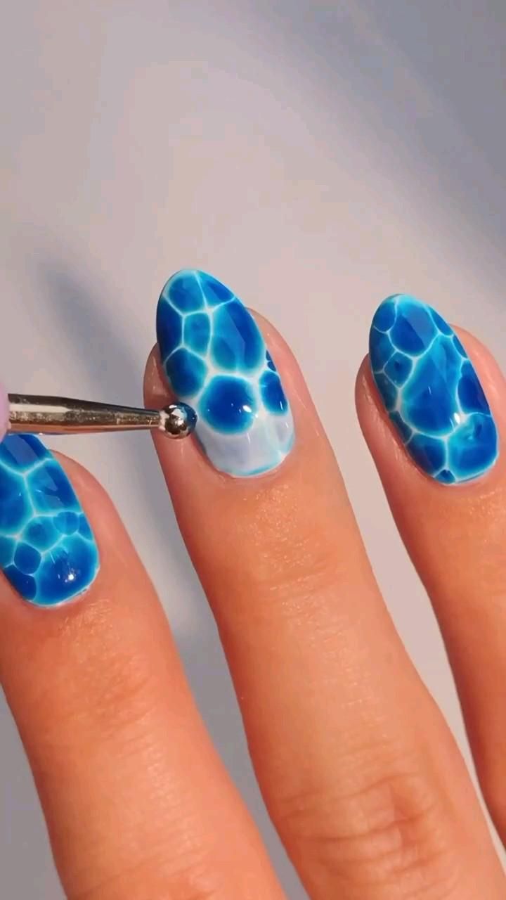 Close-up of fingers with blue and white water bubble nail art, showing a tool adding a new bubble to a nail.