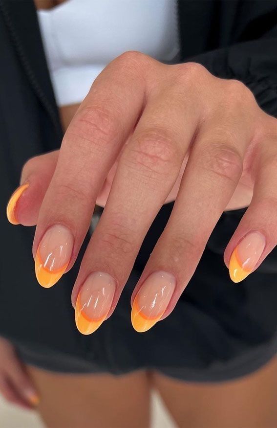 Close-up of a hand with nails featuring double French tips. The tips have an orange line at the free edge, topped with a yell
