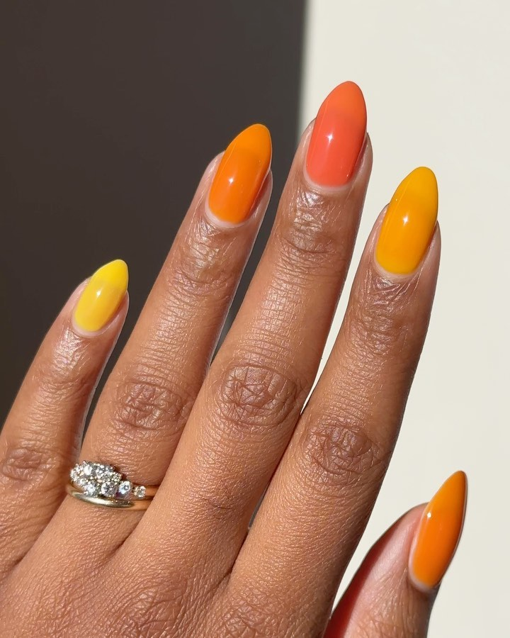 Close-up of a hand with long, glossy almond-shaped nails alternating between bright yellow and sunny orange colors.