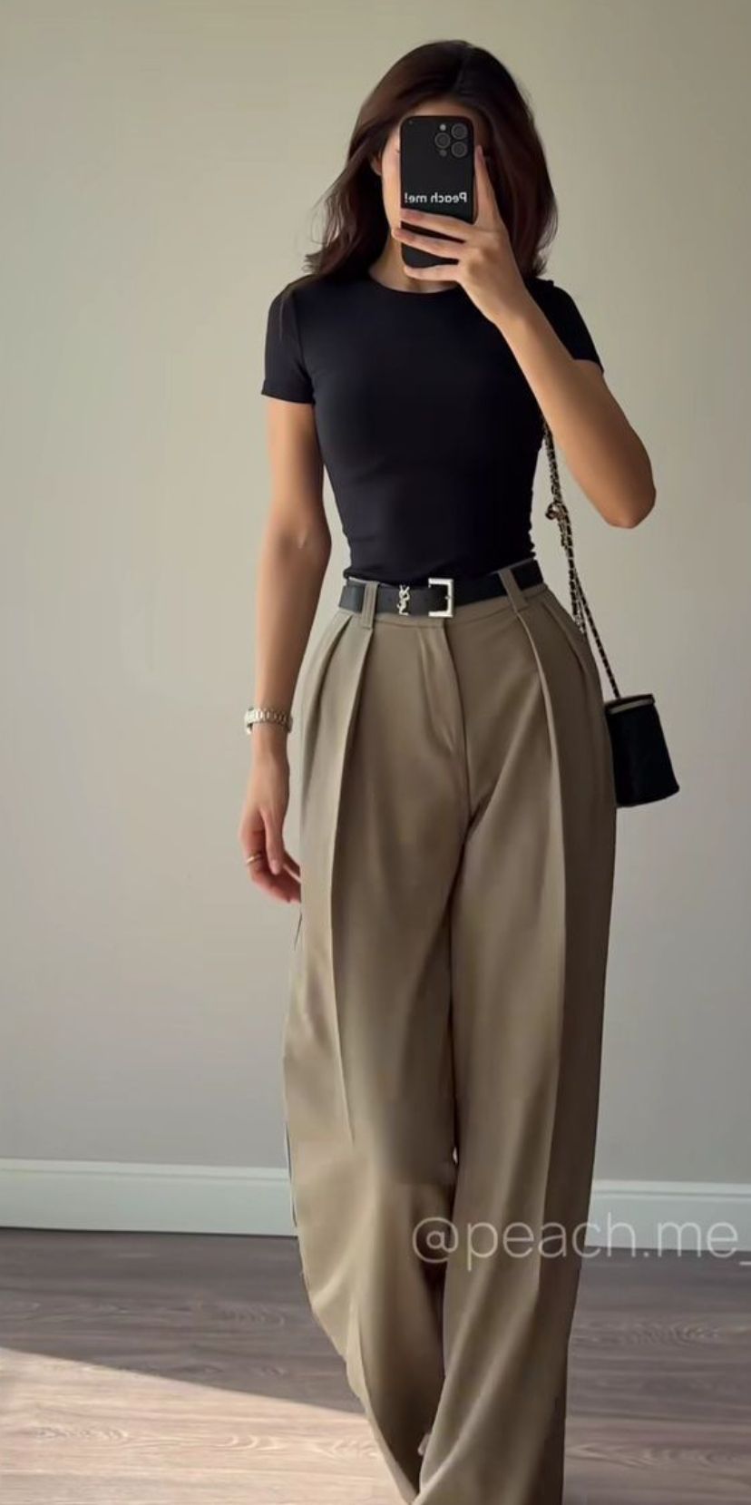 An anonymous person models wide-leg pleated khaki trousers styled with a black tee, black belt, and black shoulder bag.