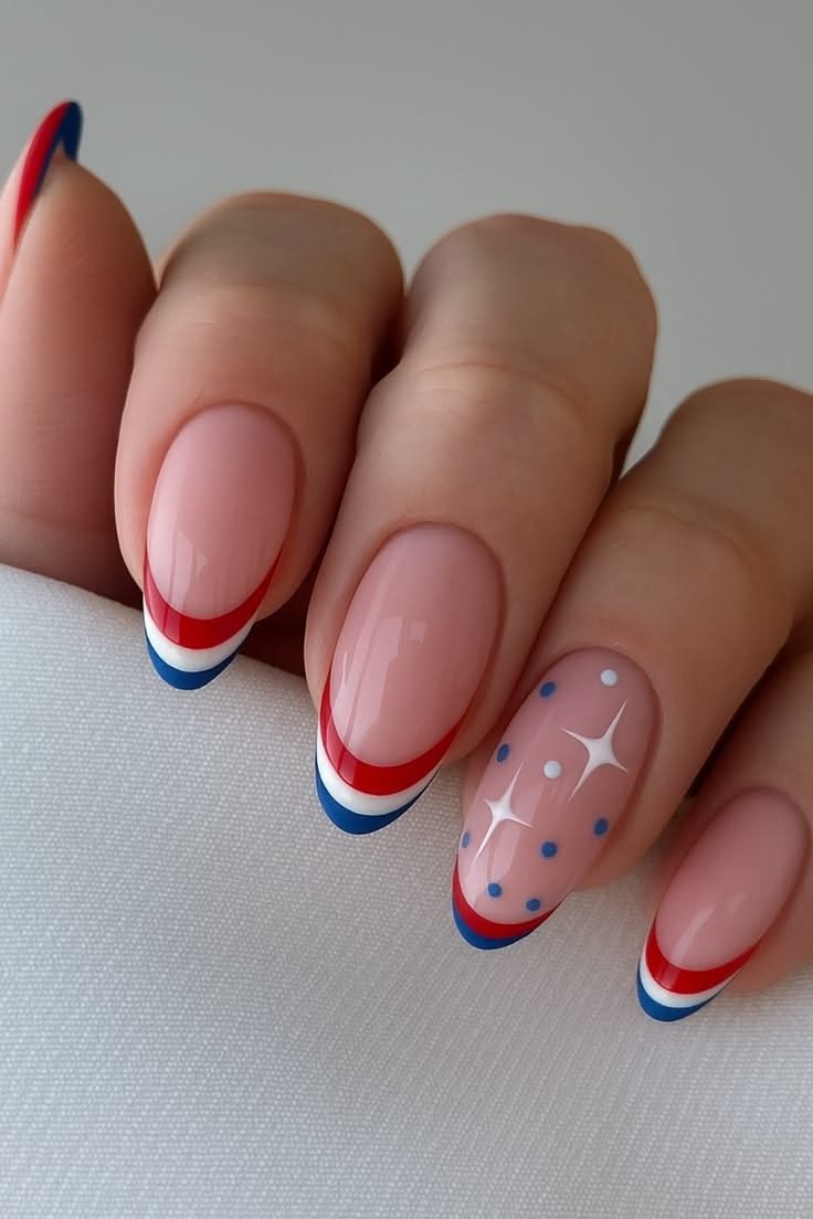 Close-up of a hand with nails designed to be patriotic French tips, featuring red, white, and blue bands and a ring finger…