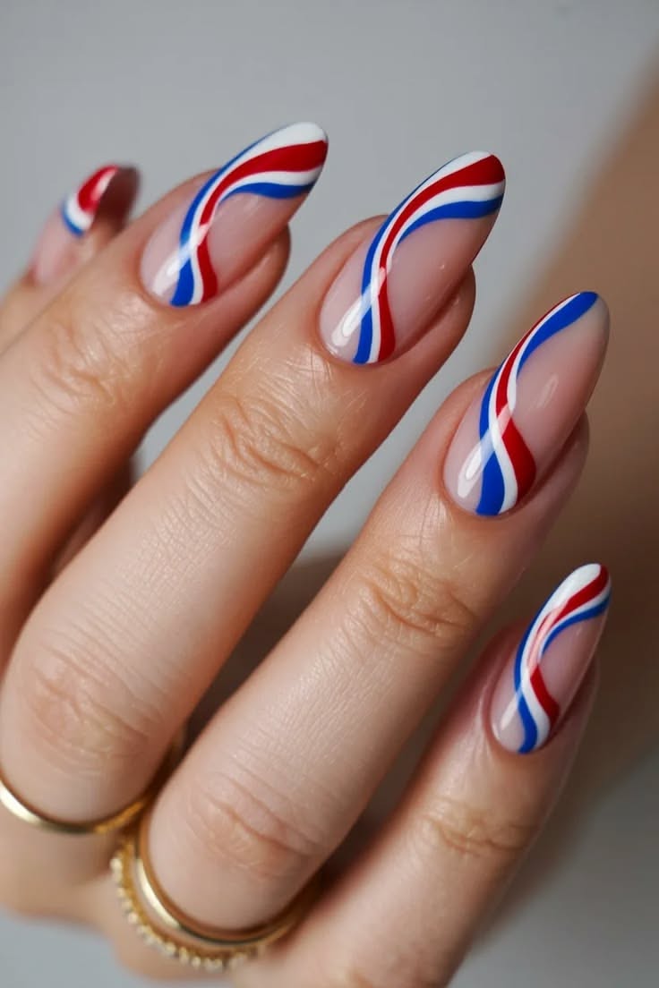 Close-up of a hand with almond-shaped nails featuring red, white, and blue wavy lines over a natural base.