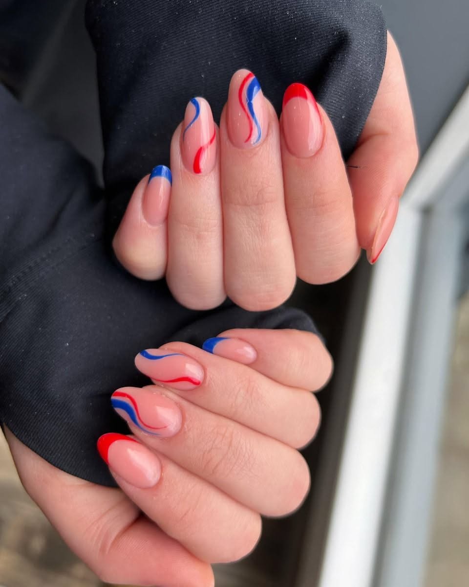 Close-up of hands with patriotic nail art, featuring wavy red and blue lines on a clear base and solid red and blue tips.