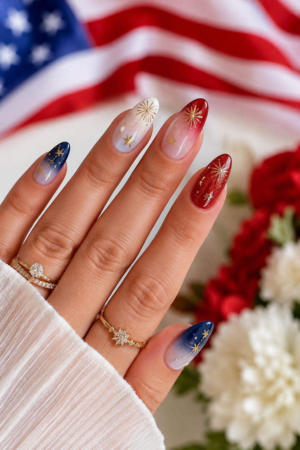 Almond-shaped red, white, and blue ombre nails with gold glitter, metallic stars and starbursts