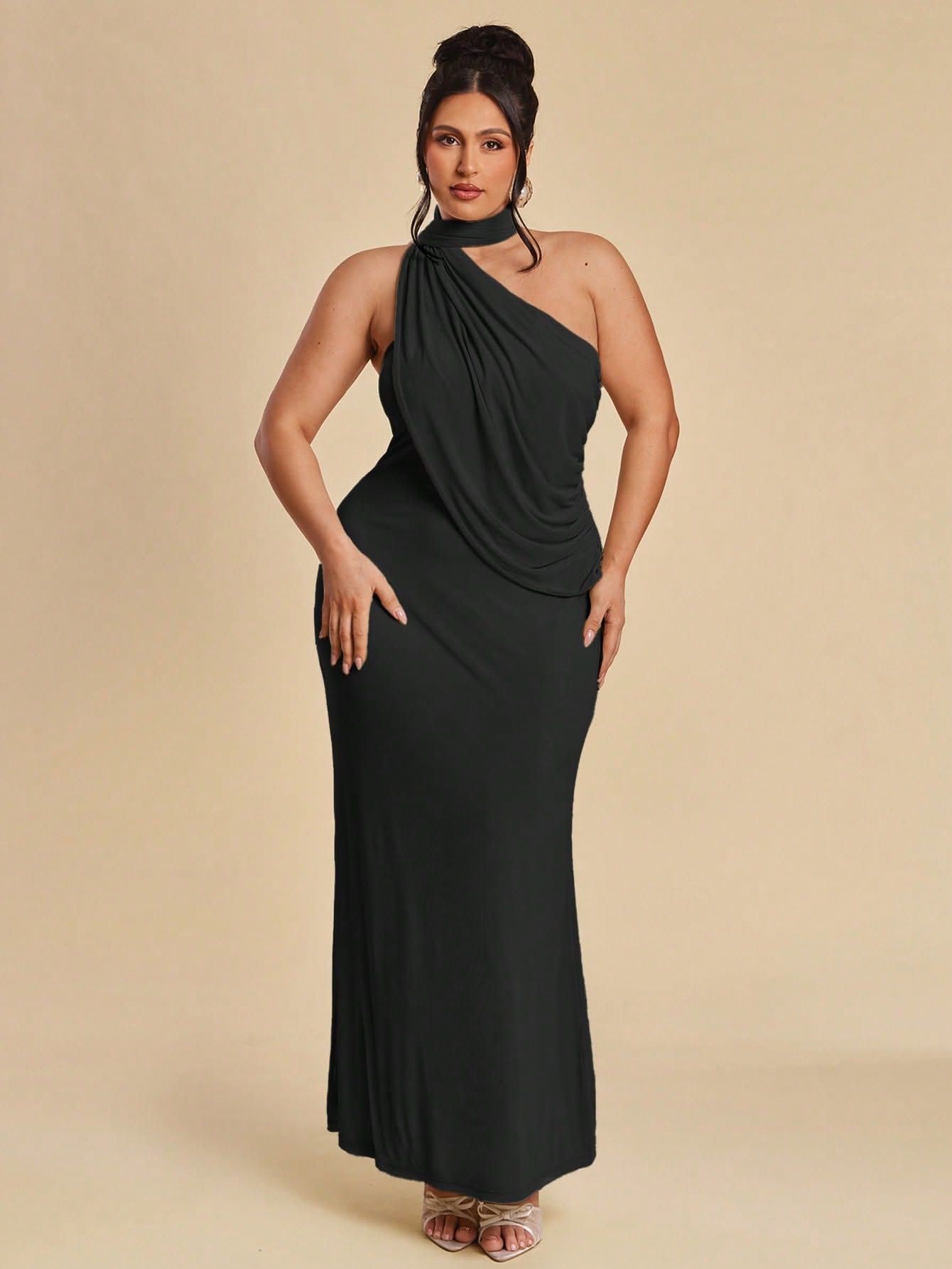 A person wears a one-shoulder floor-length black dress with a ruched bodice and a high neckline, paired with gold…